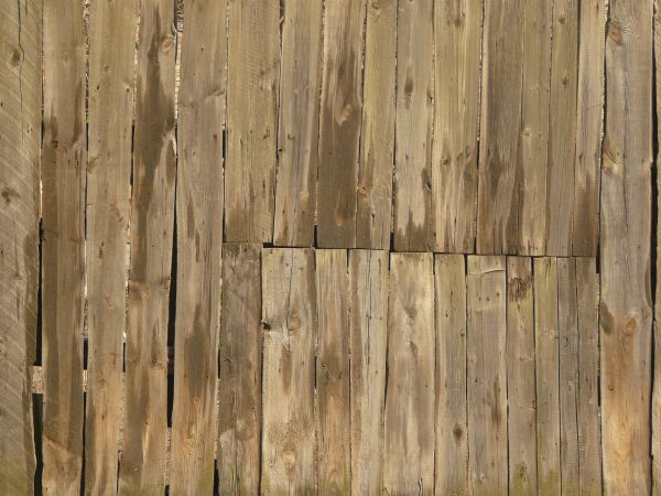 Uneven brown planks with crooked edges and dark spots set vertically with large gaps in between.